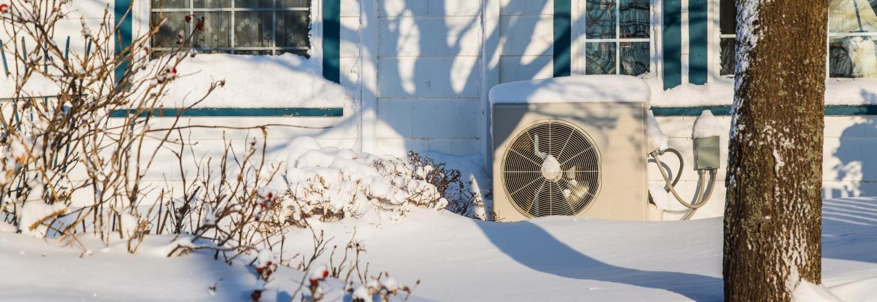 outdoor heat pump unit covered in snow outside of a home