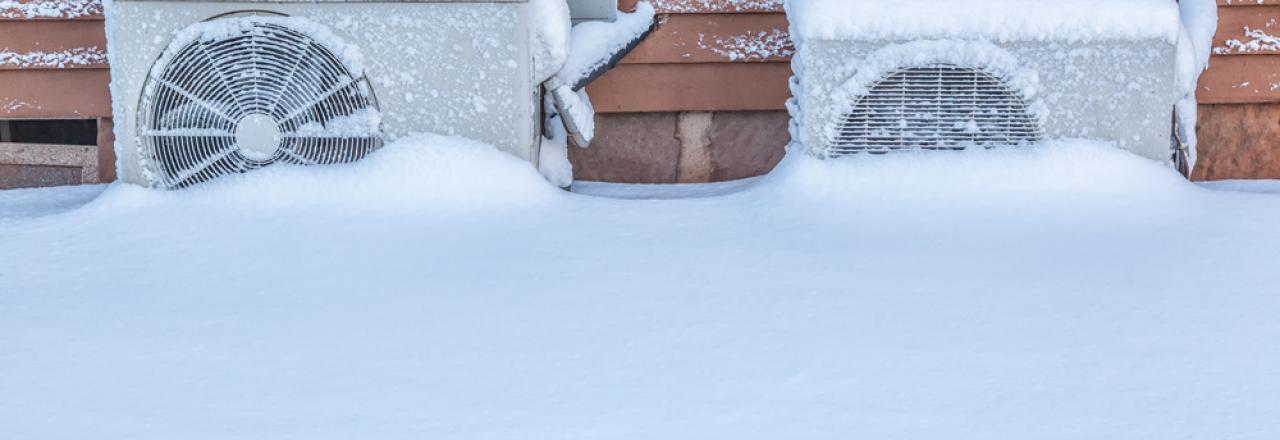 Two exterior residential heat pumps buried in snow