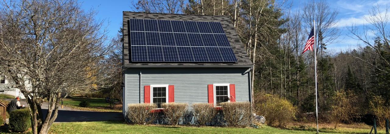 image depicting solar array on roof against blue sky and green grass